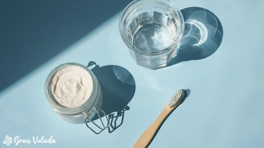 Un bocal en verre contenant du dentifrice artisanal à côté d’un verre d’eau et d’une brosse à dents en bambou.